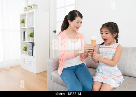 Jolie mère élégante donnant la crème glacée dessert pour jolie petite fille de beauté au cours de l'été quand ils assis sur le sofa du salon. Banque D'Images