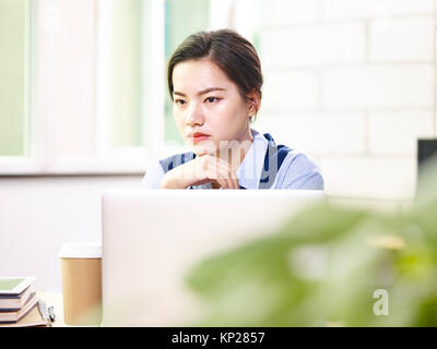 Young Asian business woman sitting in front of laptop computer pense en bureau. Banque D'Images
