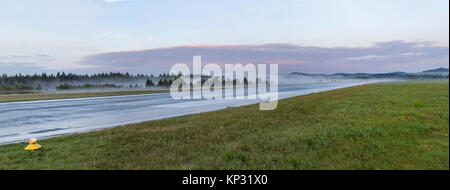 La piste de l'aéroport à vide au cours d'un lever de soleil brumeux. La piste de brouillard. Banque D'Images