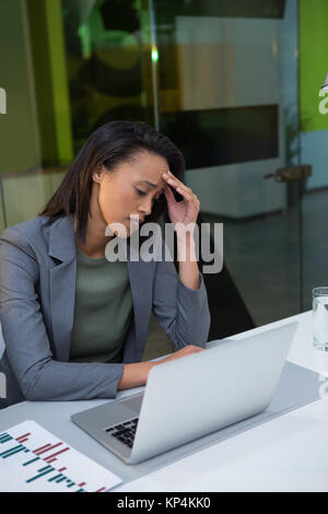 Tendu businesswoman using laptop at desk in office Banque D'Images