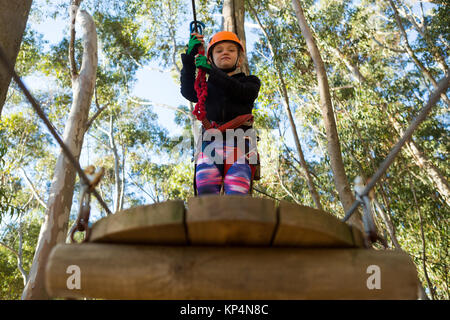 Little girl wearing helmet holding rope et debout sur la plate-forme en bois dans la forêt Banque D'Images