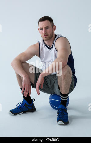 Joueur de basket-ball assis sur ball against white background Banque D'Images