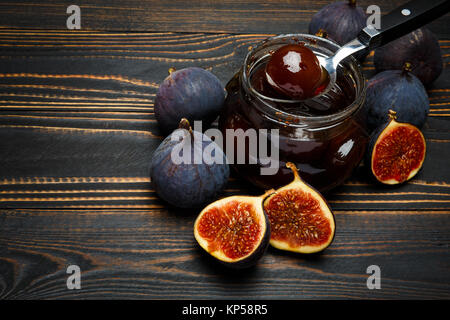 Pots de verre remplis de confiture de figue et figue fruits sur une base en bois foncé Banque D'Images