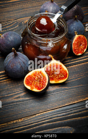 Pots de verre remplis de confiture de figue et figue fruits sur une base en bois foncé Banque D'Images