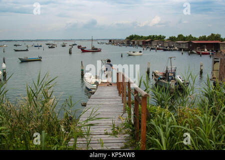 Paysage du lac avec un garçon sur une jetée en bois entouré de bateaux de pêche. Parc du Delta du Po lagon. Veneto, Italie. Banque D'Images