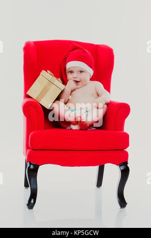 Bébé, 4 Monate, Weihnachtsmuetze und mit sitzt auf einem roten Meteo Contactez-Stuhl - Noël bébé assis sur une chaise rouge Banque D'Images