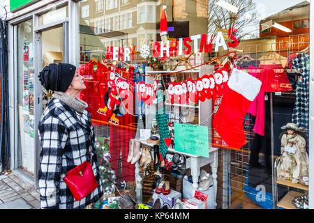 Femme plus âgée à la recherche dans la fenêtre de l'Hospice du nord de Londres magasin de charité dans Fortis Green Road, Muswell Hill, London, UK, à l'approche de Noël Banque D'Images