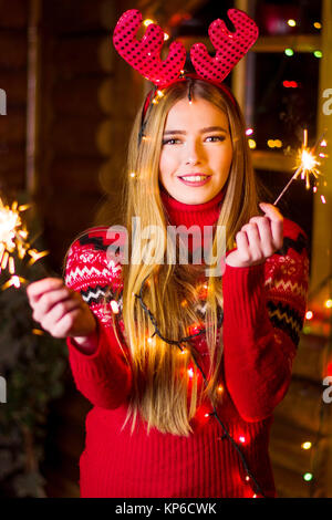 Belle fille avec lumières de fête wearing red sweater dans une maison en bois rond Banque D'Images