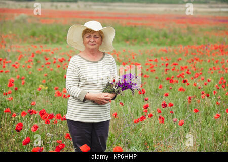 La femme âgée dans une prairie de coquelicots Banque D'Images