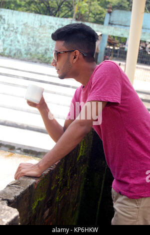 Jeune modèle masculin debout sur balcon avec une tasse de café. Banque D'Images