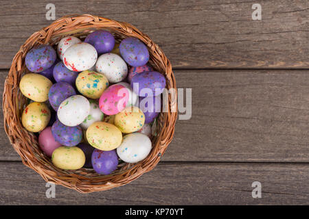 Oeufs de Pâques colorés de bonbons dans un panier sur une surface en bois Banque D'Images