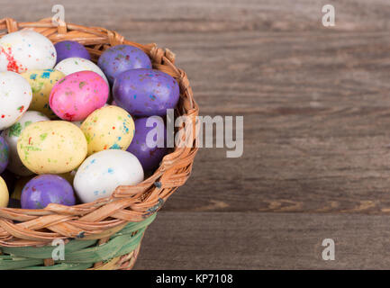 Libre d'oeufs de Pâques colorés de bonbons dans un panier sur une surface en bois Banque D'Images