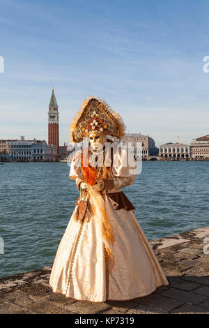 Carnaval de Venise, Vénétie, Italie 2017 femme en costume et un masque orange classique au coucher du soleil avec le palais des Doges derrière sur lagoon Banque D'Images