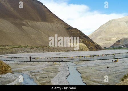 Trekker debout sur un pont suspendu traversant la rivière Kali Gandaki. Ville de Kagbeni visible dans la distance, la région de Mustang (Népal). Banque D'Images