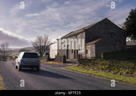 Voiture (Land Rover Discovery) voyageant passé pierre, route barn & bâtiments agricoles on country road - Barden, Yorkshire, Angleterre, Royaume-Uni. Banque D'Images