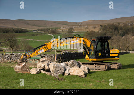 Pelle à chenilles jaune vif JCB JS130LC située dans un champ de campagne agricole, prête à soulever des blocs lourds - Kilnsey, Yorkshire Dales, Angleterre, Royaume-Uni. Banque D'Images