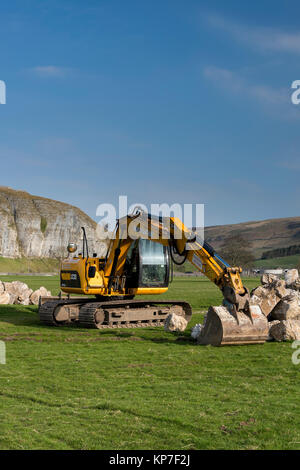 Pelle à chenilles jaune vif JCB JS130LC située dans un champ de campagne agricole, prête à soulever des blocs lourds - Kilnsey, Yorkshire Dales, Angleterre, Royaume-Uni. Banque D'Images