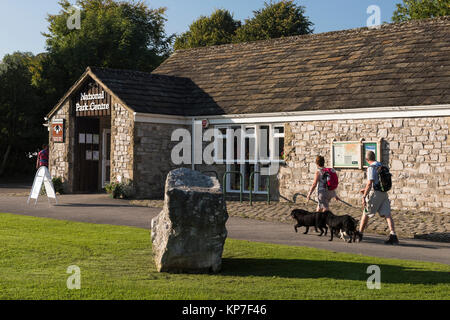 Sunny, journée d'automne, vue extérieure du Centre des Visiteurs du Parc National, avec couple de marcheurs et 2 chiens, en passant - Malham, Yorkshire, Angleterre, Royaume-Uni. Banque D'Images