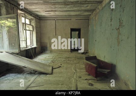 Dans la salle en ruine maison abandonnée à Pripyat, fauteuil rouge près du mur avec le vol du plâtre, de la poussière, de Tchernobyl, en Ukraine. Banque D'Images