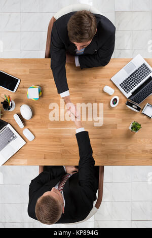 Businessmen Shaking Hands At Desk In Office Banque D'Images