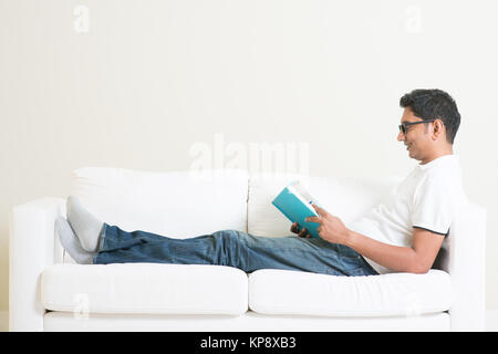 Asian man reading book on couch Banque D'Images