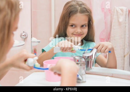 Happy little girl serre les dents d'un tube sur une brosse à dents Banque D'Images