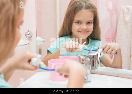 Six ans, fille serre les dents d'un tube sur une brosse à dents Banque D'Images