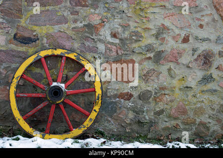 Ancienne roue de chariot en bois sur un mur en pierre en hiver Banque D'Images