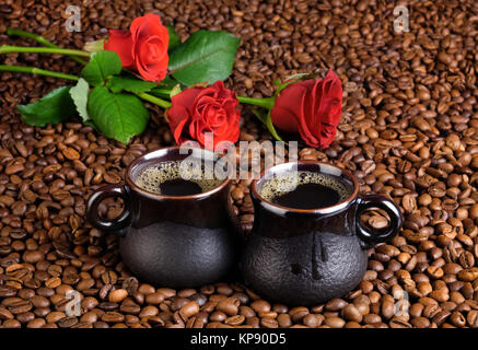 Deux tasses de café noir sur l'arrière-plan de les grains de café et une roses rouges. Banque D'Images