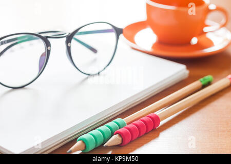 Crayons et lunettes sur ordinateur portable blanc vierge ouvert avec tasse de café sur le bureau Banque D'Images