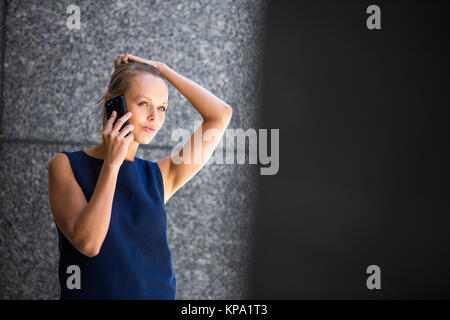 Jolie jeune businesswoman talking on the phone en face d'un immeuble moderne à Manhattan (shallow DOF (tons de couleur libre) Banque D'Images