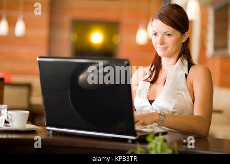 Communiqué de modèle, Junge Frau sitzt im Kaffeehaus an der Theke und arbeitet suis coffre - young woman using laptop in cafeteria Banque D'Images