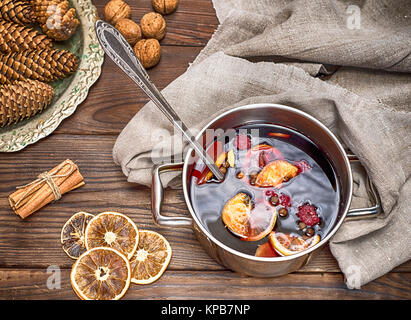 Vin chaud dans un pot avec poignées et ingrédients pour faire une boisson alcoolisée faite maison sur un fond en bois brun Banque D'Images