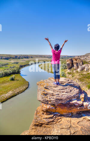 Woman raising hands en haut d'un Hoodoo le long de la rivière Milk au parc provincial Writing-on-Stone en Alberta, Canada. La zone contient le plus grand conc Banque D'Images