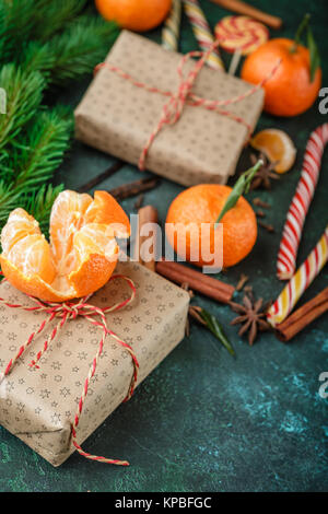 Mandarines fraîches avec des feuilles, des cannes de bonbon, boîtes-cadeaux dans du papier kraft et épices - cannelle, d'anis et de girofle sur un fond vert foncé Banque D'Images