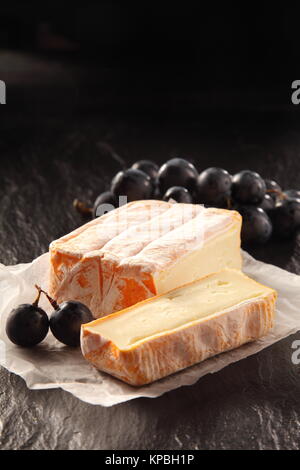 Close Up de bloquer des fromages vieillis avec fin coupé sur morceau de papier ciré avec Dark Red Grapes on the Rough Surface texturée Banque D'Images