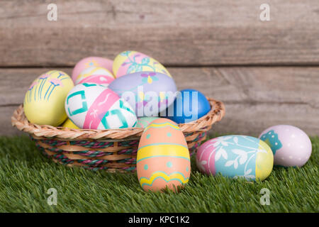 Les oeufs de Pâques colorés et panier sur l'herbe contre un arrière-plan bois Banque D'Images