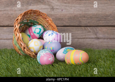 Les oeufs de Pâques colorés à partir d'un panier renversé sur l'herbe contre un arrière-plan bois Banque D'Images