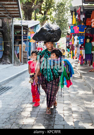 PANAJACHEL, GUATEMALA-DEC 24, 2015 : : Guatamalian femme avec deux enfants transporter sur sa tête grand sac noir le Déc 24, 2015 à Panajachel, Guatemala. Banque D'Images