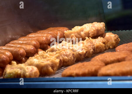 Une sélection ou variété d'aliments frits dans un présentoir de comptoir tiède ou chaude dans un poisson et chip shop. saucisses et battues fishcakes ordinaire garder chaud. Banque D'Images