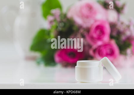 Un pot de crème sur la table,à l'arrière-plan un grand bouquet,qui se déplie sa beauté. merveilleux tons rose est sur la table Banque D'Images