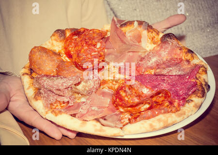 Les hommes&# 39 s mains tiennent italien pizza au jambon et salami Banque D'Images