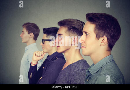 Vue latérale des quatre jeunes hommes debout en ligne et à l'avant sur fond gris. Banque D'Images