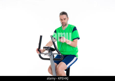 Jeune homme en chemise verte avec la machine de remise en forme et using smartphone Banque D'Images