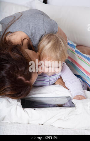 Mère embrassant bébé regardant tablet Banque D'Images