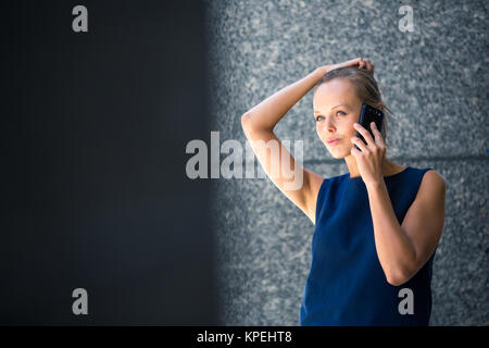 Jolie jeune businesswoman talking on the phone en face d'un immeuble moderne à Manhattan (shallow DOF (tons de couleur libre) Banque D'Images