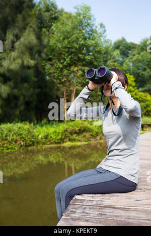 Young Woman sitting on wooden path et l'utilisation des jumelles Banque D'Images