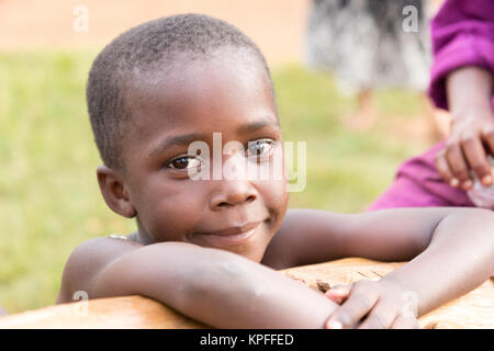 Lugazi, en Ouganda. 18 juin 2017. Une belle petite fille s'appuyant sur un tronc de bois. Banque D'Images