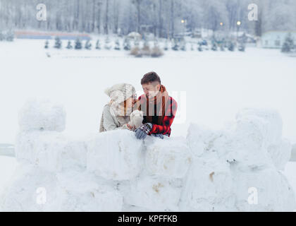 Close-up portrait horizontal de l'heureux couple parler et rire tout en s'appuyant sur le mur de neige dans le village. Banque D'Images