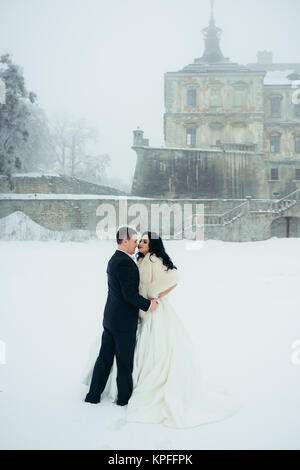 Pleine longueur verticale tourné de l'amour couple hugging tendrement sur la prairie enneigée près de la vieille maison. Banque D'Images